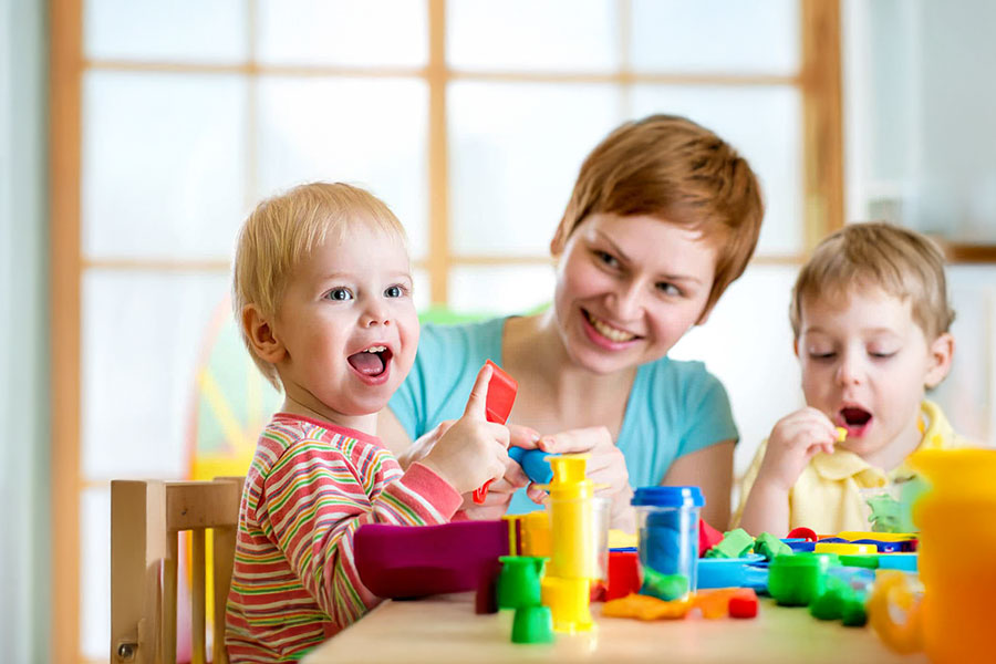 mom of two sittinng between her children who are happily playing with toys on a table, early signs of autism representation