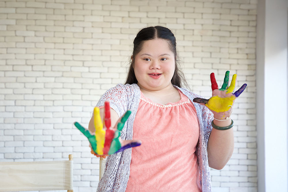 down syndrome teenage girl showing painted hands, drawing a picture on paper at an NPS